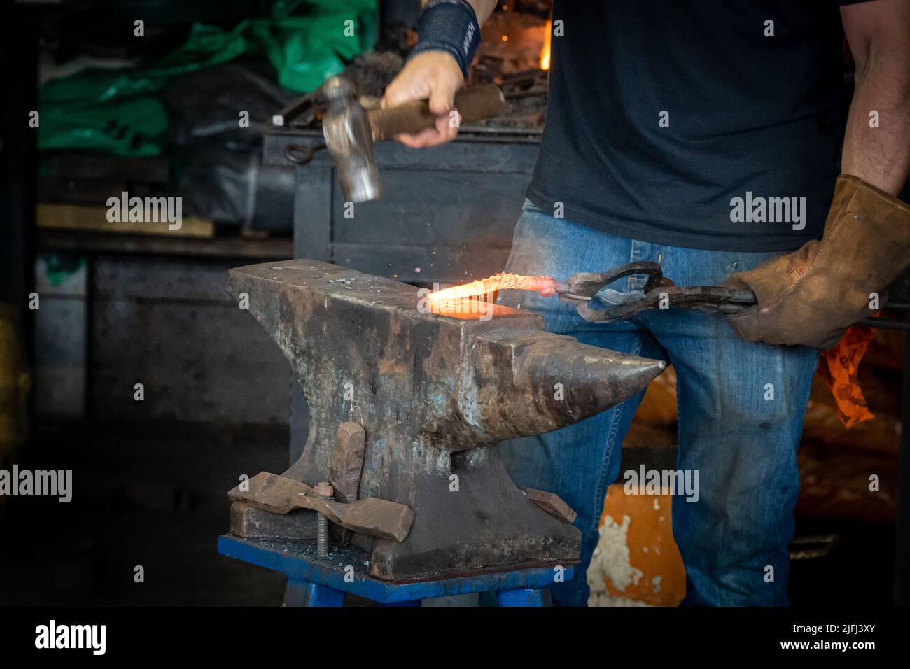 Nahaufnahme der Hände eines Schmieds mit einem Hammer und Amboss, um einen rotheißen Eisenrohling zu Formen Stockfoto