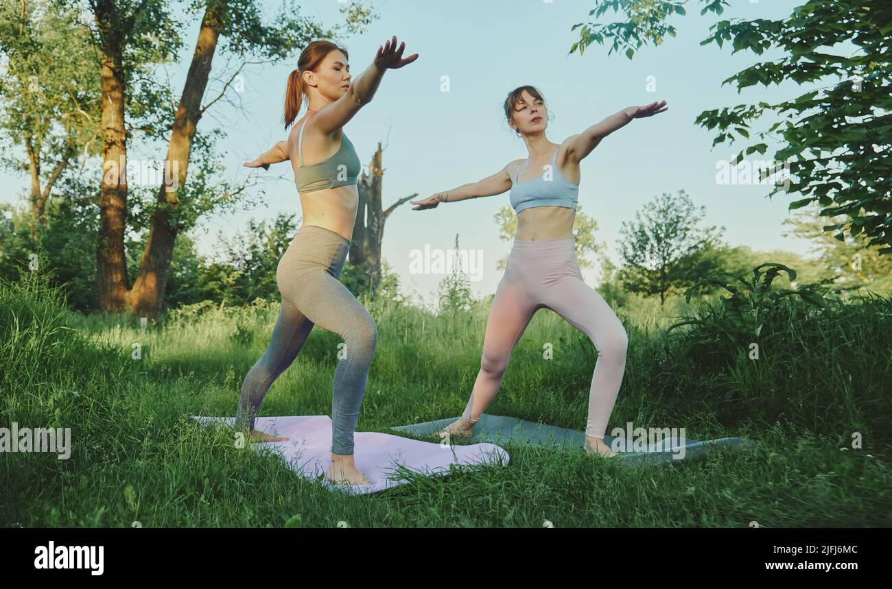 Zwei junge Frauen machen Yoga virabhadrasana im Freien Stockfoto