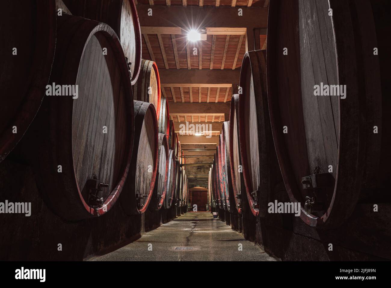 Reihen von hölzernen, mit Wein gefüllten Fässern säumen den Keller des Weinguts, ein Weinkeller mit langer Tradition und Geschichte Stockfoto