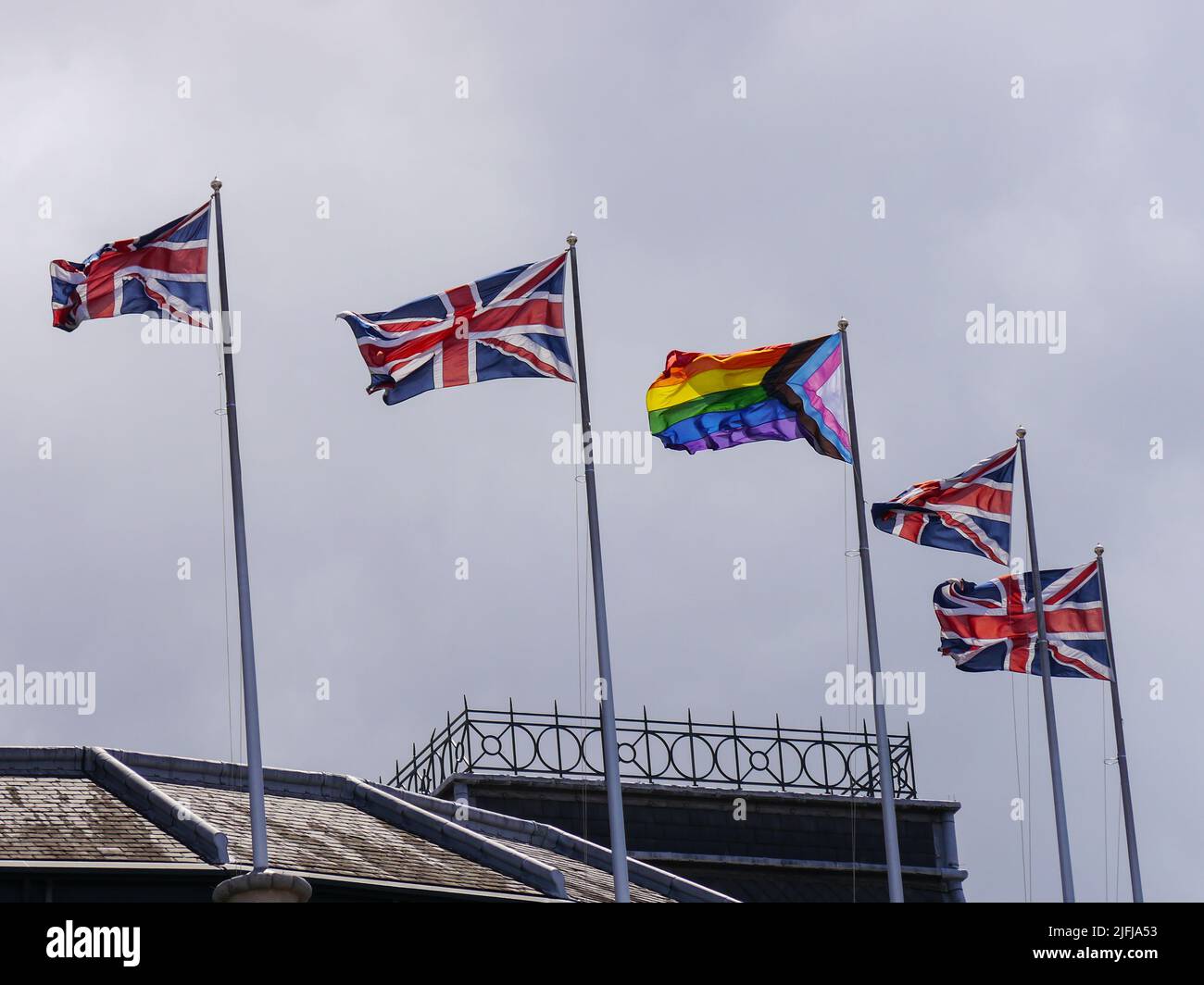 Die LGBTQ-Flagge fliegt zwischen zwei Gewerkschaftsflaggen auf Fahnenmasten Stockfoto