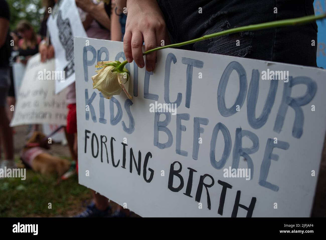 Kansas City, Missouri, USA. 2.. Juli 2022. Ein Protestler hält eine Rose und ein Schild mit der Aufschrift „Schützen Sie unsere Kinder, bevor Sie eine Geburt erzwungen haben“, während Tausende am Samstag durch Grand Boulveard zum Mill Creek Park marschieren, um gegen den SCOTUS-Umstürzen von Roe gegen Wade zu protestieren. Missouri war der erste von 13 Staaten, der nach Roe gegen Wade, das Abtreibung auf staatlicher Ebene Verbot, die „Auslösergesetze“ erlassen hat. (Bild: © Luke Townsend/ZUMA Press Wire) Stockfoto