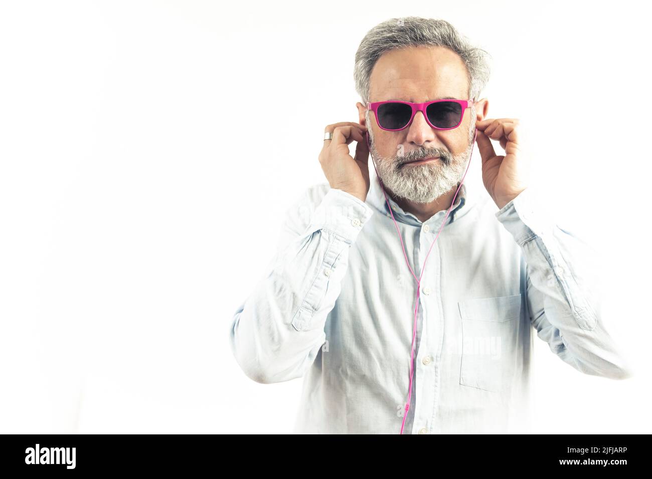 Grauhaarige kaukasischen Mann in rosa Sonnenbrille hört Musik in rosa Kopfhörer weißen Hintergrund Studio Schuss Kopie Raum drinnen . Hochwertige Fotos Stockfoto