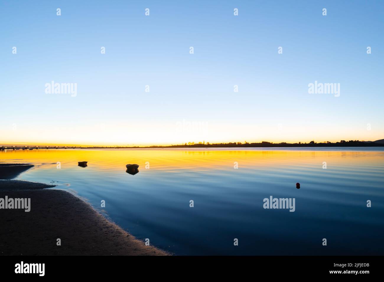 Der Sonnenaufgang am Hafen von Tauranga mit Blau- und Goldtönen über der ruhigen Bucht mit Wellen, die sich am Strand abwaschen. Stockfoto