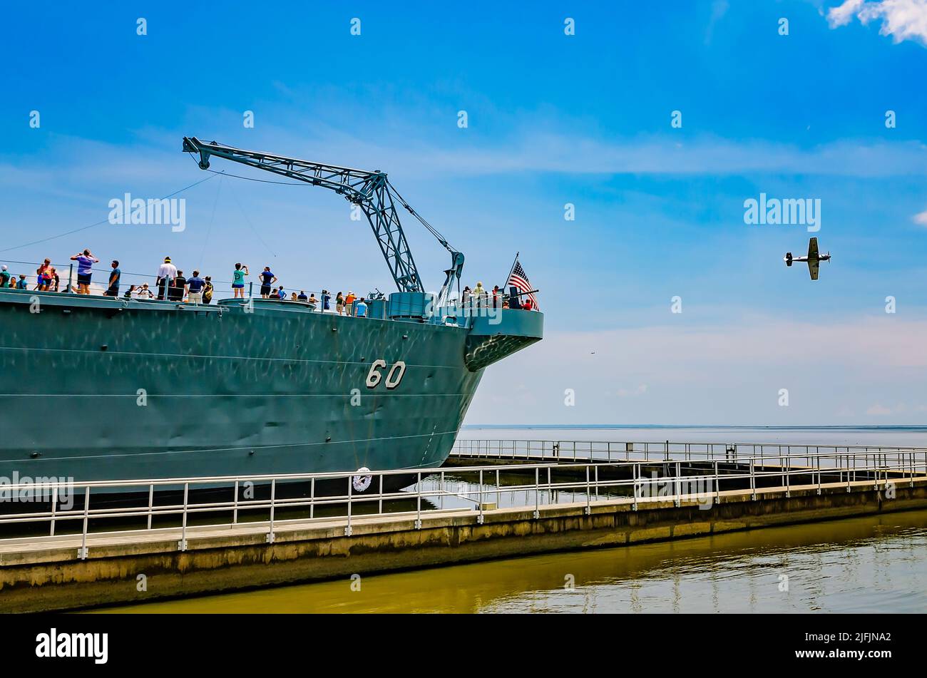 Am 12. August 2017 fliegt ein altes Kampfflugzeug im Battleship Memorial Park in Mobile, Alabama, vorbei und die Menschen erkunden das Deck der USS Alabama. Stockfoto