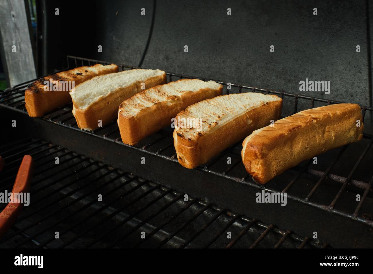 Hot Dog Buns liegen auf ihrer Seite, während sie auf dem oberen Gestell eines Grills geröstet werden. Stockfoto