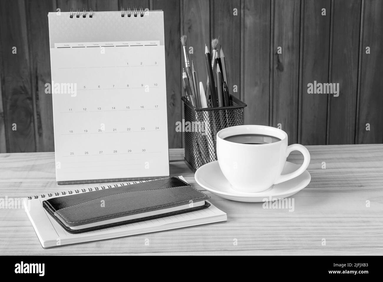 Schwarz-weißes Notizbuch, Kaffeetasse und Bücherstapel mit Kalender auf Holztisch-Hintergrund. Geschäftskonzept Stockfoto