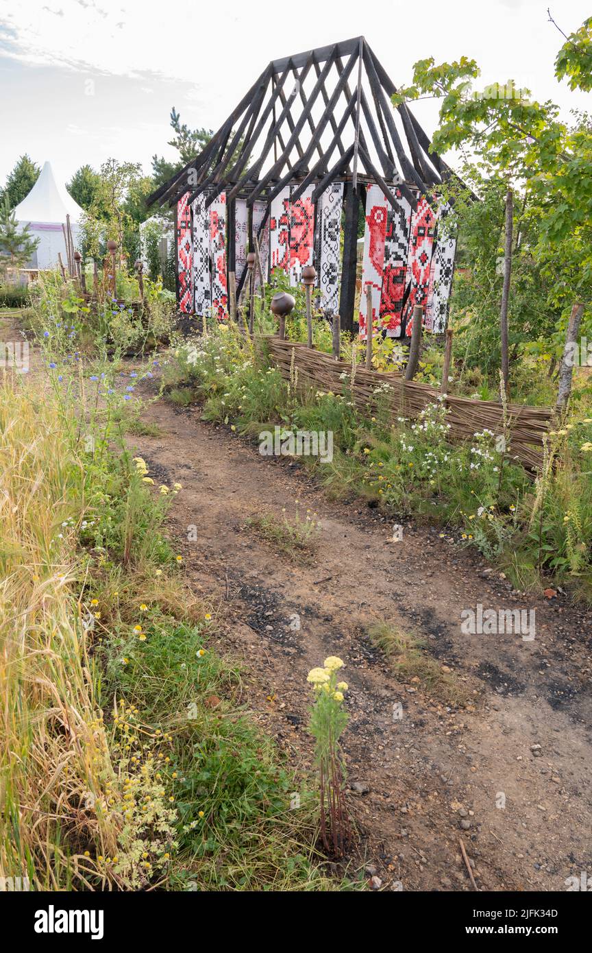 Hampton Court Palace, Surrey, Großbritannien. 4. Juli 2022. RHS Hampton Court Palace Garden Festival Pressetag für die größte Blumenschau der Welt, die bis zum 9. Juli 2022 stattfindet. Bild: Global Impact Garden: What does Not Burn Entworfen von Victoria Manoylo und Carrie Preston ist eine Destillation der ukrainischen Landschaft und Kultur. Es zeigt den Rushnyk, ein besticktes Tuch, das in vielen Ritualen verwendet wird, als Symbol des Lebens und der Identität. Wie eine neue Haut schmücken Rushnyks die Überreste einer verbrannten Hütte, die als Silhouette in der Landschaft steht. Quelle: Malcolm Park/Alamy Live News Stockfoto
