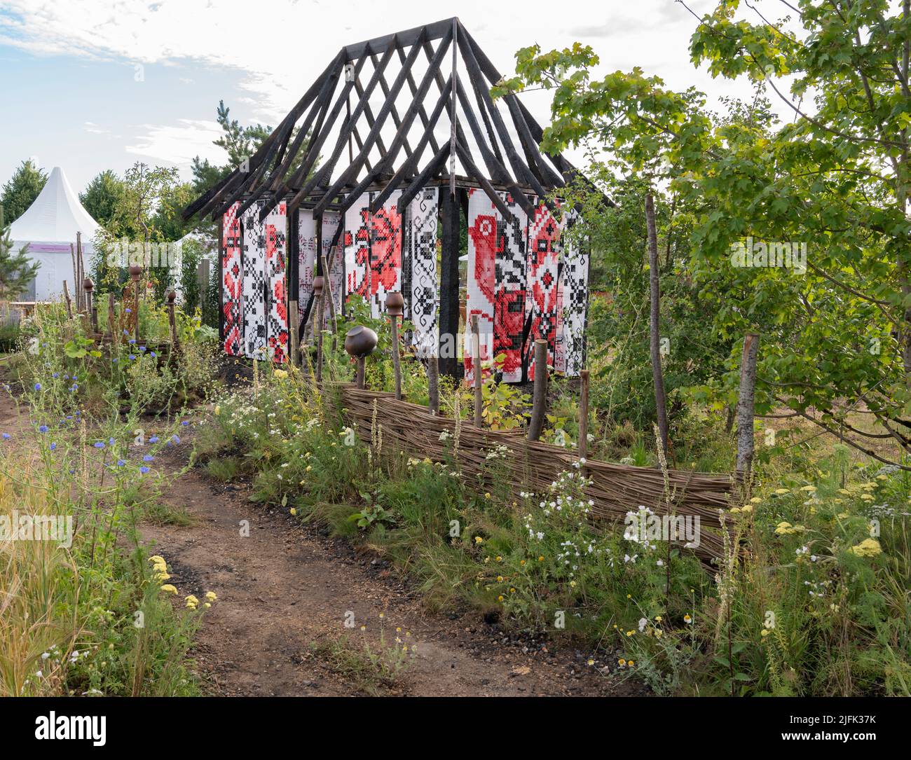 Hampton Court Palace, Surrey, Großbritannien. 4. Juli 2022. RHS Hampton Court Palace Garden Festival Pressetag für die größte Blumenschau der Welt, die bis zum 9. Juli 2022 stattfindet. Bild: Global Impact Garden: What does Not Burn Entworfen von Victoria Manoylo und Carrie Preston ist eine Destillation der ukrainischen Landschaft und Kultur. Es zeigt den Rushnyk, ein besticktes Tuch, das in vielen Ritualen verwendet wird, als Symbol des Lebens und der Identität. Wie eine neue Haut schmücken Rushnyks die Überreste einer verbrannten Hütte, die als Silhouette in der Landschaft steht. Quelle: Malcolm Park/Alamy Live News Stockfoto