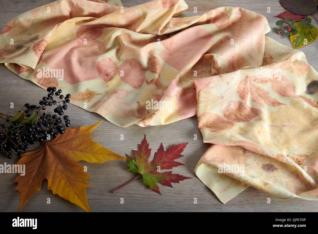 Handgefärbter Seidenschal, umgeben von Beeren und Herbstblättern. Eco-Print-Technik Stockfoto