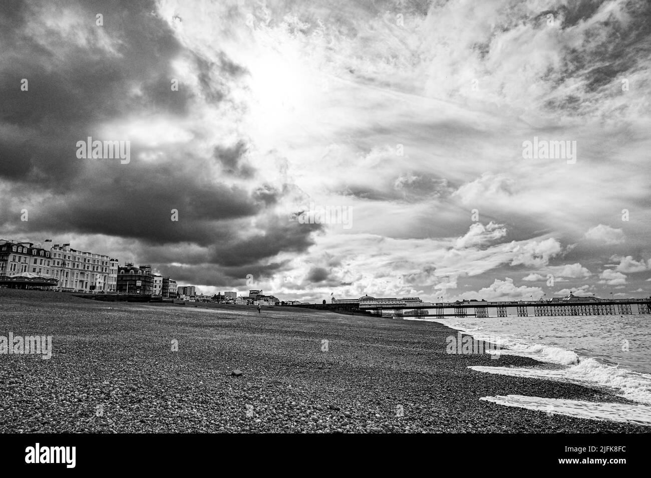 Brighton , Sussex , England Großbritannien - Dunkle Wolken über der Strandpromenade von Brighton und dem Strand mit der Sonne, die versucht, durchzubrechen Stockfoto