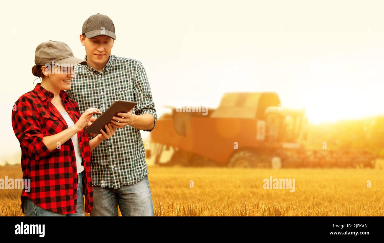 Zwei Landwirte mit digitalem Tablet auf dem Hintergrund des Mähdreschers. Smart Farming-Konzept. Stockfoto