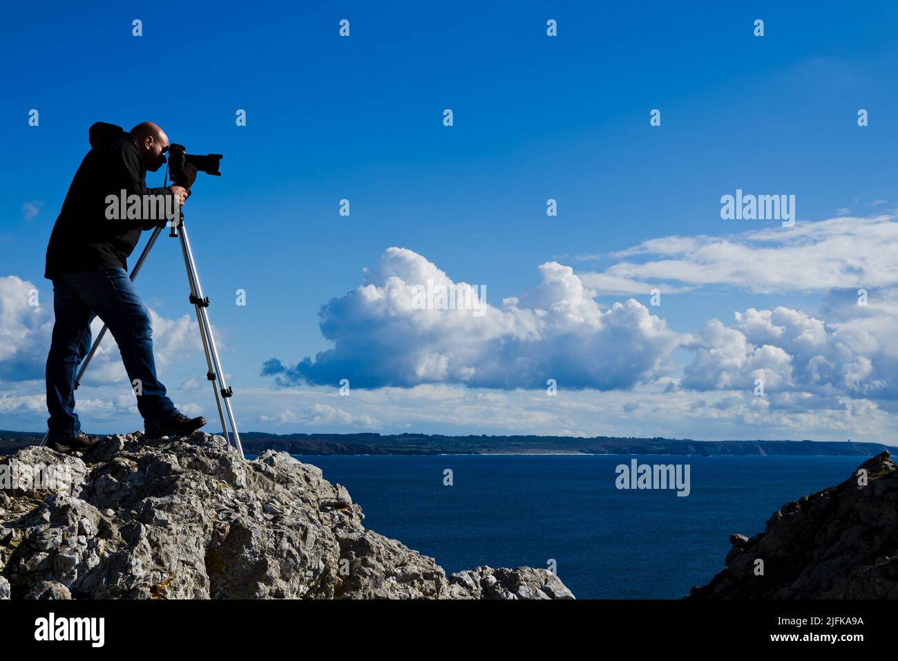 Outdoor-Fotograf, der auf einem Felsen steht und Fotos von der atemberaubenden Landschaft der Bretagne in der Nähe von Pointe de Penhir fotografiert. Stockfoto