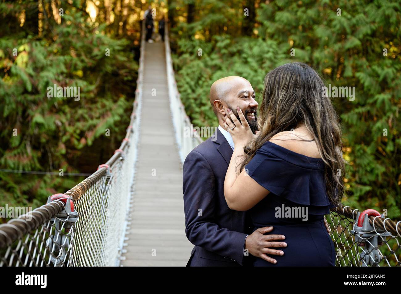 Voller Liebe Foto eines liebevollen gemischten jungen Paares, das sich auf einer Hängebrücke im Lynn Canyon Park, North Vancouver, hält, Stockfoto