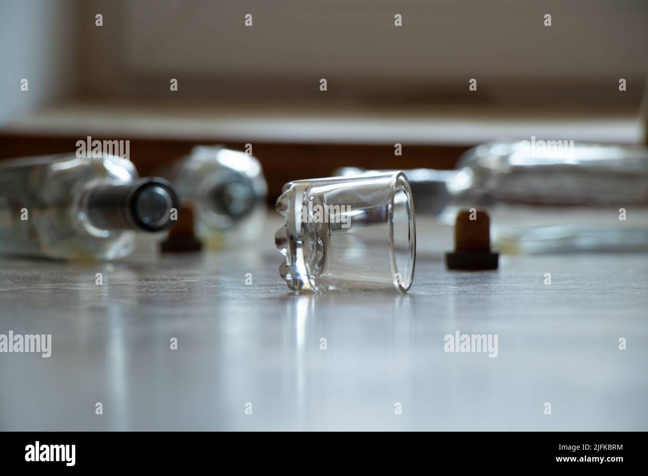 Ein Glas und leere Alkoholflaschen liegen auf dem Boden in einer Wohnung im Dunkeln, Alkoholismus und schlechte Gewohnheiten, Glasflaschen und ein Glas Wodka Stockfoto