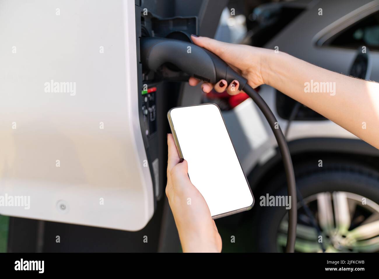 Hände mit Smartphone und Ladestecker auf einem Hintergrund von Elektroauto . Weißer Bildschirm, können Sie hier Ihre Inhalte hinzufügen Stockfoto