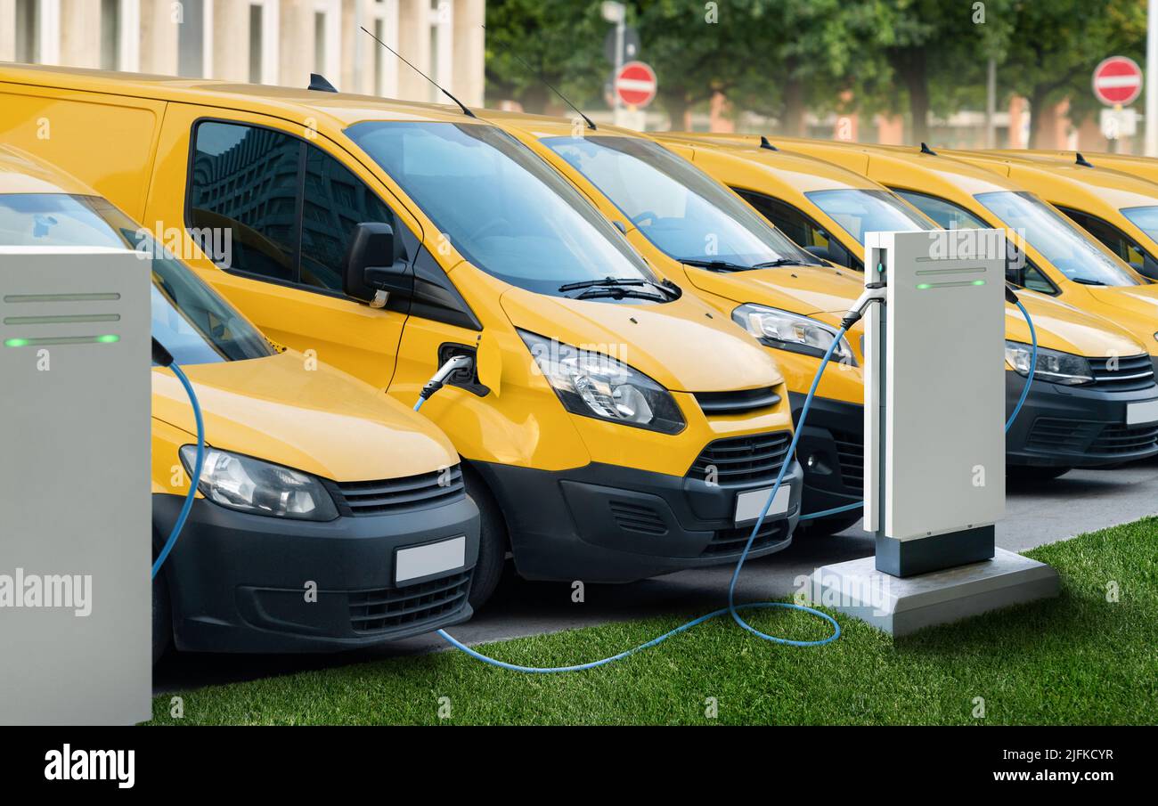 Reihe gelber elektrischer Lieferwagen an Ladestationen für Elektrofahrzeuge Stockfoto