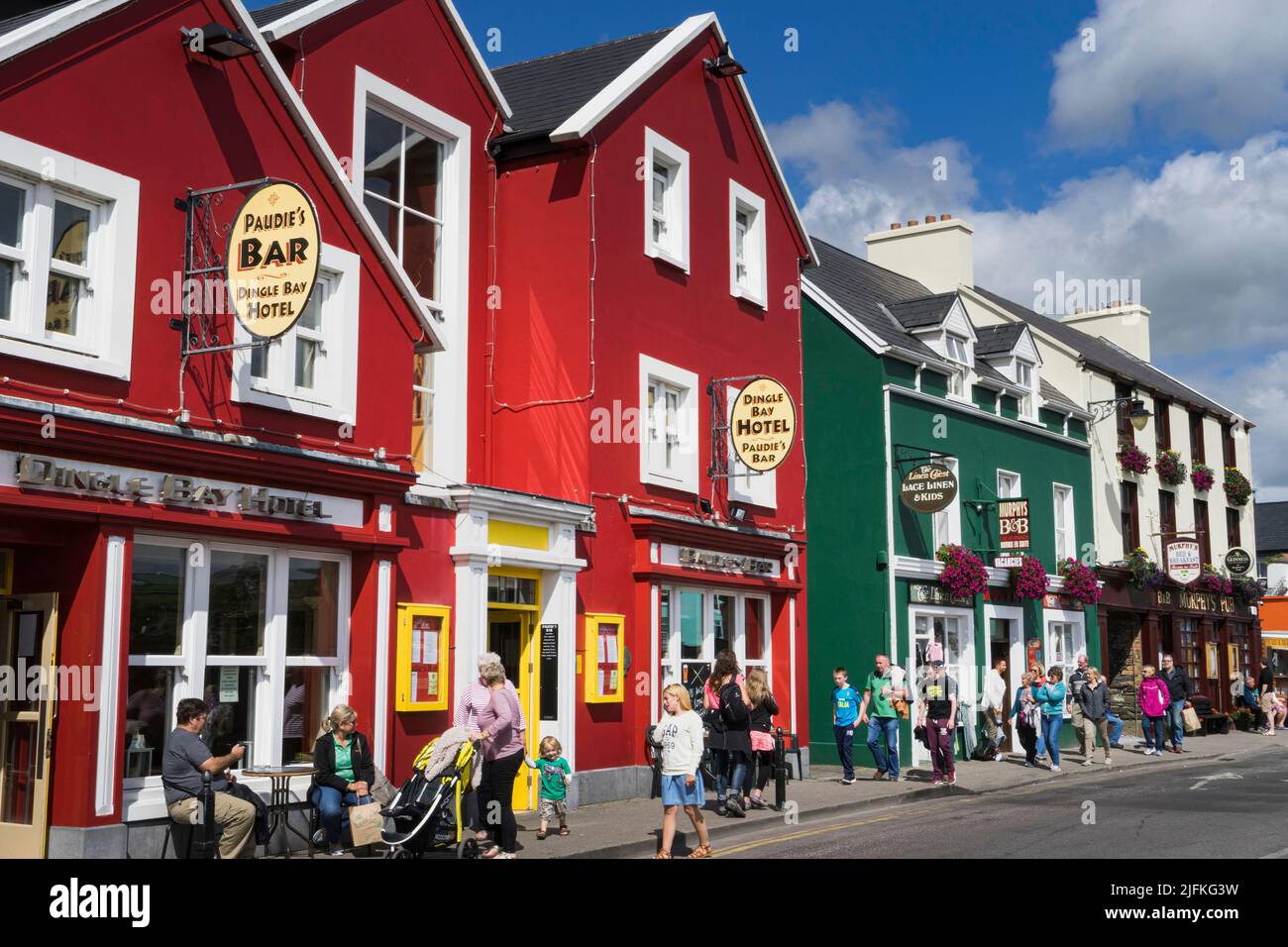 Blick auf eine Straße in der irischen Touristenstadt Dingle im Sommer, mit Pub und Hotel im Vordergrund und typischen Häusern in roten und grünen Farben. Stockfoto