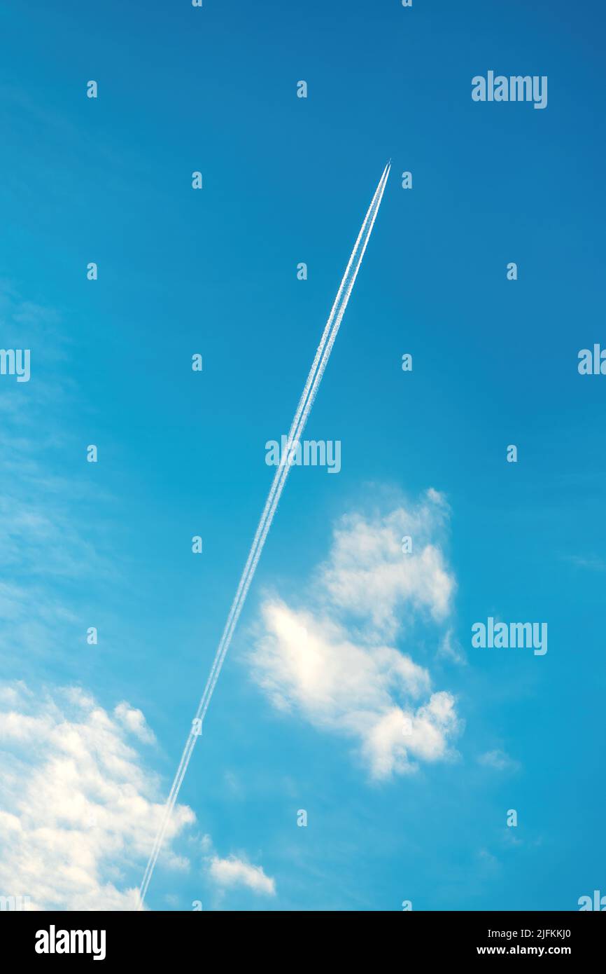 Dampfspur oder Kondensstreifen am blauen Himmel mit Wolken von unten Stockfoto
