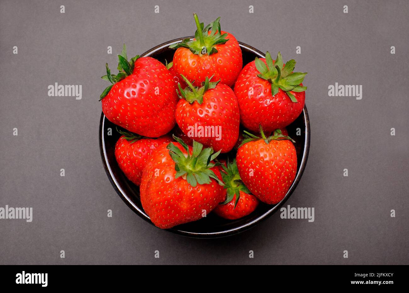 Frisch gepflückte englische Erdbeeren in einer Schüssel auf braunem Hintergrund Stockfoto