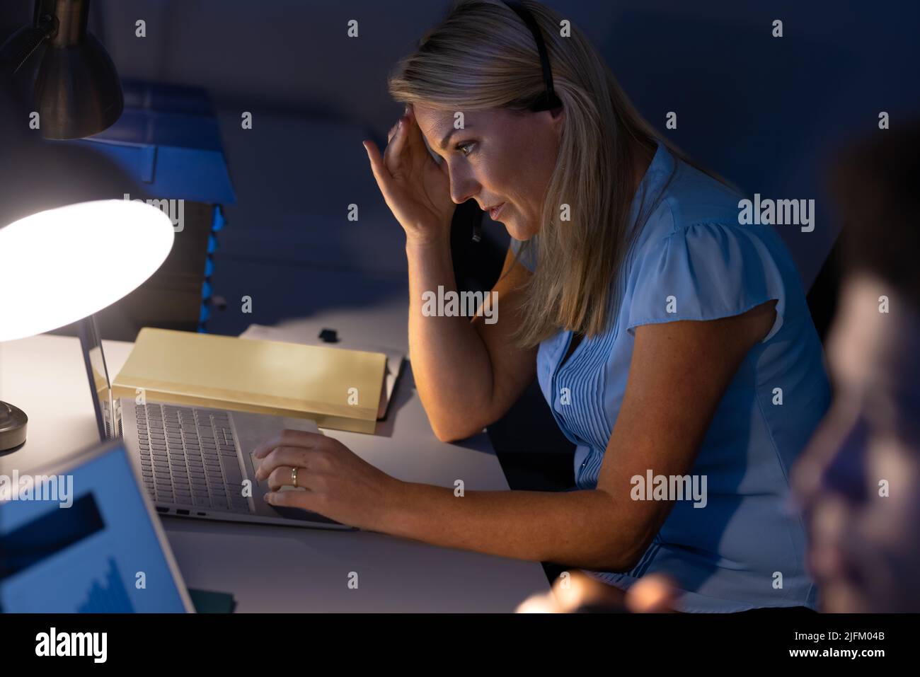 Blick auf die kaukasische Geschäftsfrau mit Kopf in der Hand, die auf dem Schreibtisch im Büro über dem Laptop arbeitet Stockfoto