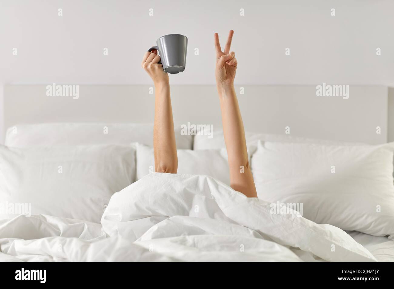 Frau mit Kaffee, der im Bett lag und Frieden zeigte Stockfoto