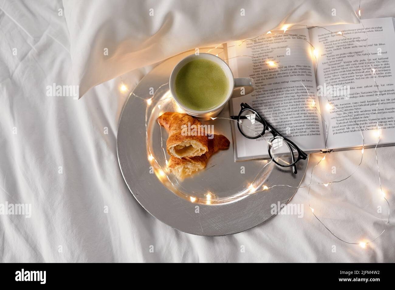Croissants, Matcha-Tee, Buch und Gläser im Bett Stockfoto