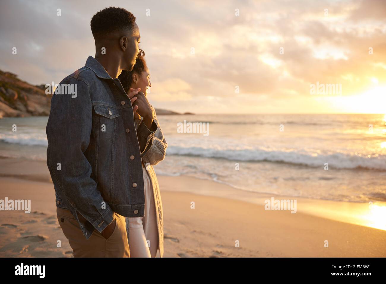Junges multiethnisches Paar, das an einem Strand spazieren geht und den Sonnenuntergang betrachtet Stockfoto