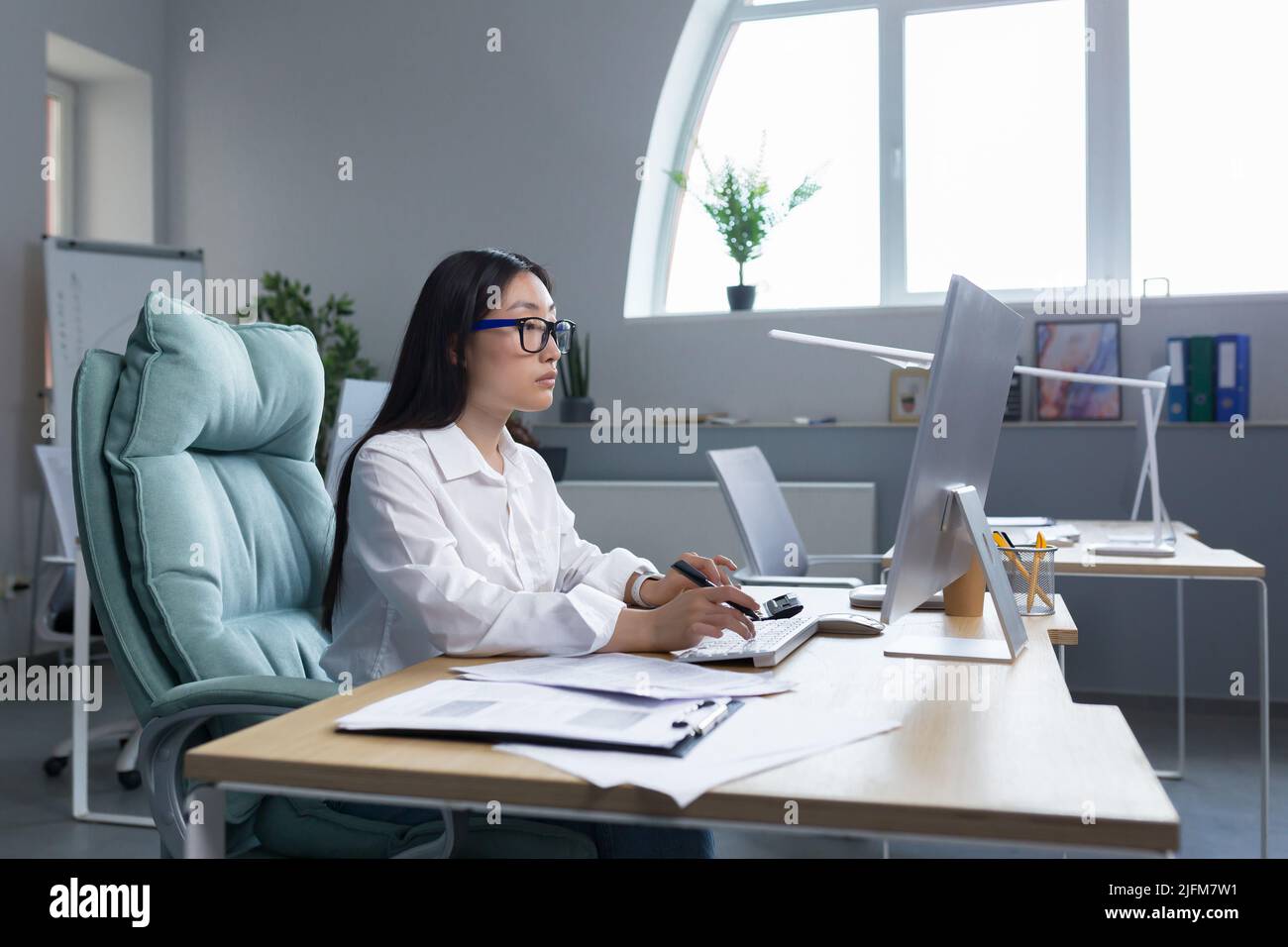 Asiatische erfolgreiche Geschäftsfrau arbeitet mit Computer in modernen Büro, nachdenklich und konzentriert. Stockfoto