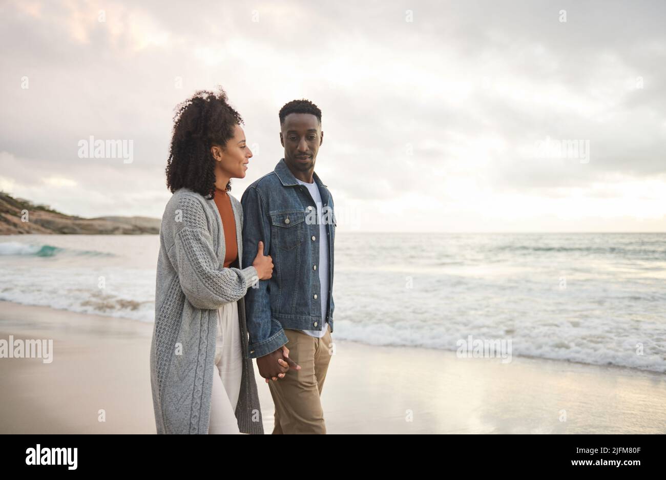 Junges multiethnisches Paar, das sich die Hände hält und an einem Sandstrand läuft Stockfoto