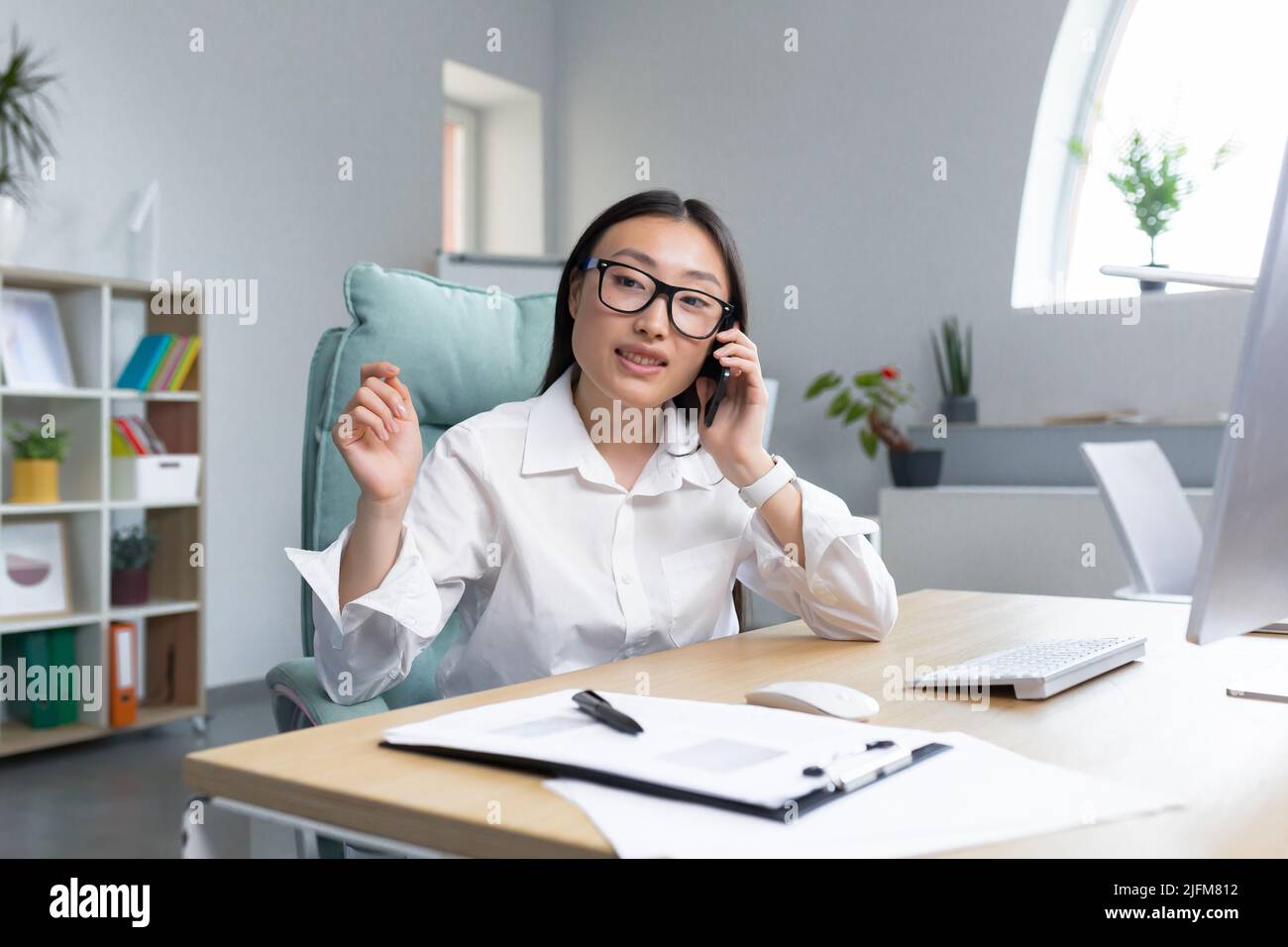 Schöne asiatische Büroangestellte Sekretärin, die in einem modernen Büro arbeitet, am Telefon lächelt und die Kamera anschaut. Stockfoto