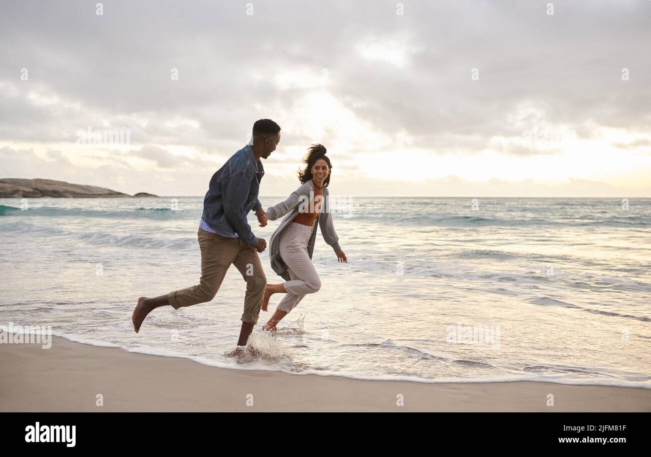 Junges multiethnisches Paar, das am Strand durch die Brandung läuft Stockfoto