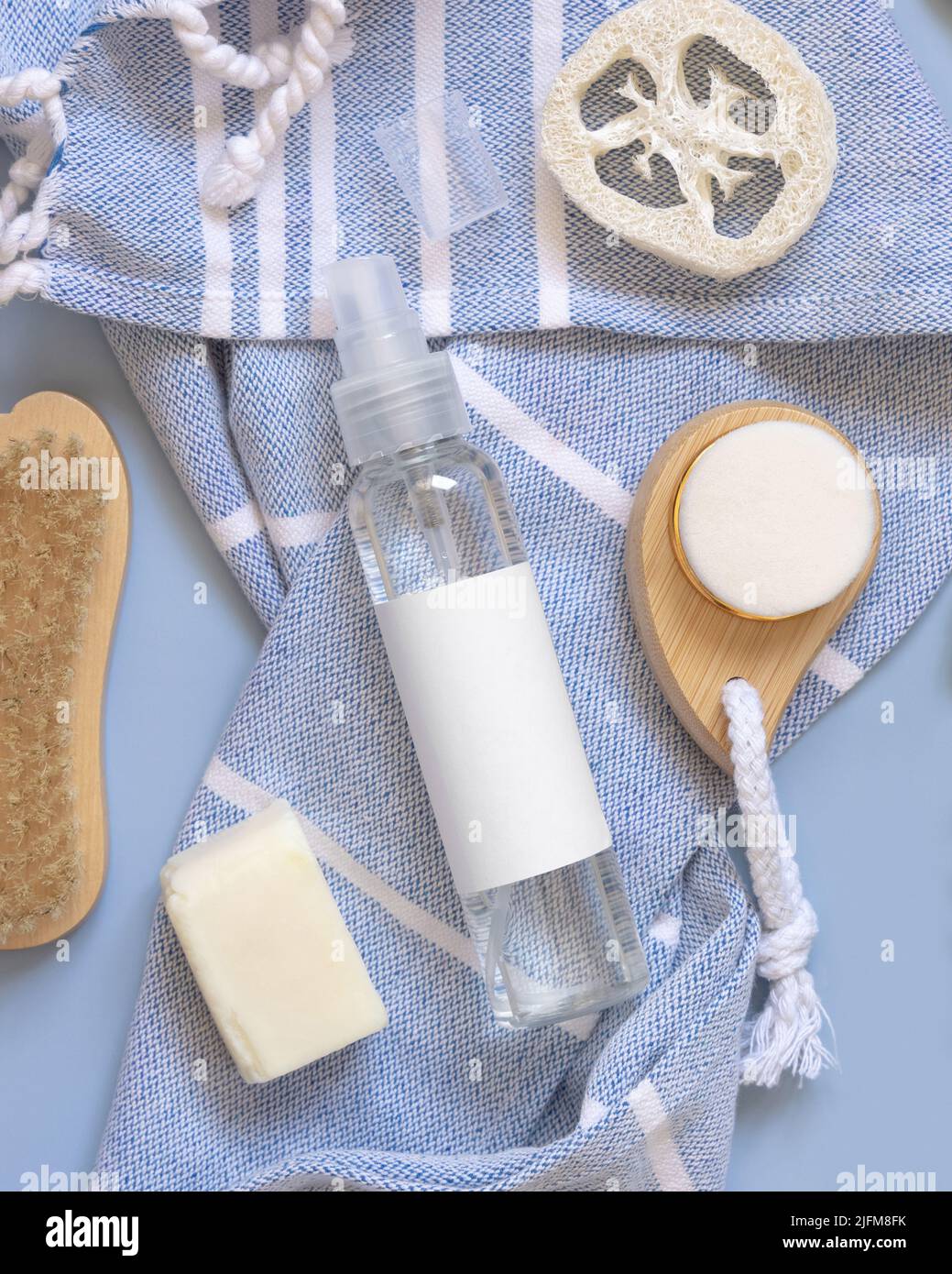 Nachfüllbare Sprühflasche, Haut- und Haarpflegezubehör auf blauem Badetuch in der Nähe tropischer Blätter Draufsicht, Kopierraum. Verpackungsmodup. Natürliches Homema Stockfoto