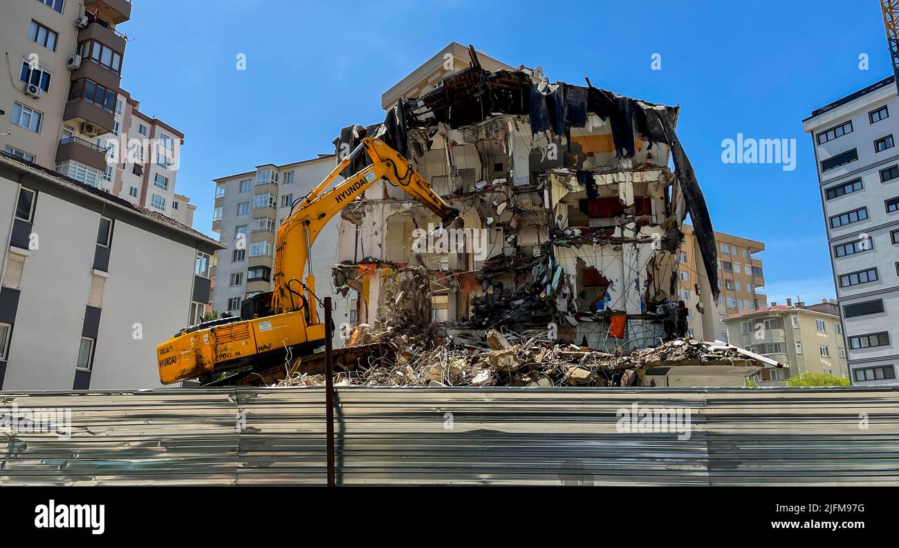 Großer gelber Bagger bricht altes Haus ab, Abriss eines Mehrfamilienhauses in einem Wohngebiet, Abriss einer Stahlbetonkonstruktion Stockfoto