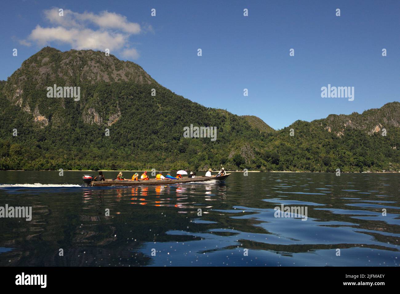 Ein Boot mit Touristen segelt auf dem Meerwasser im Hintergrund der Landschaft der Insel Seram in der Nähe des Dorfes Saleman in Nord-Seram, Zentral-Maluku, Maluku, Indonesien. Stockfoto