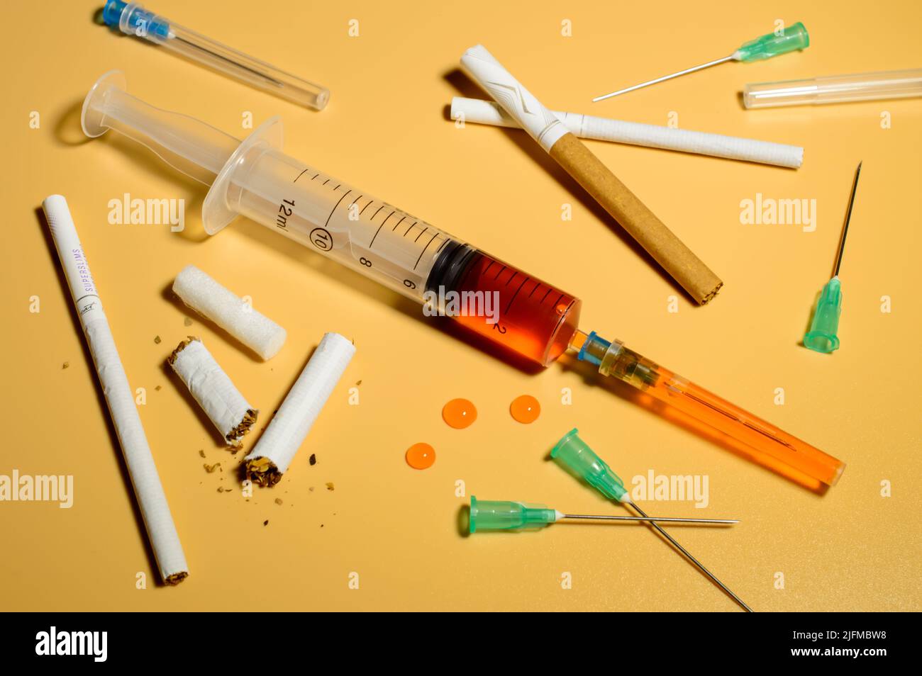 Soziale Probleme - Zusammenstellung von Zigaretten und Spritzennadeln. Spritze mit dem Medikament in der Mitte. Orangefarbener Hintergrund. Stockfoto