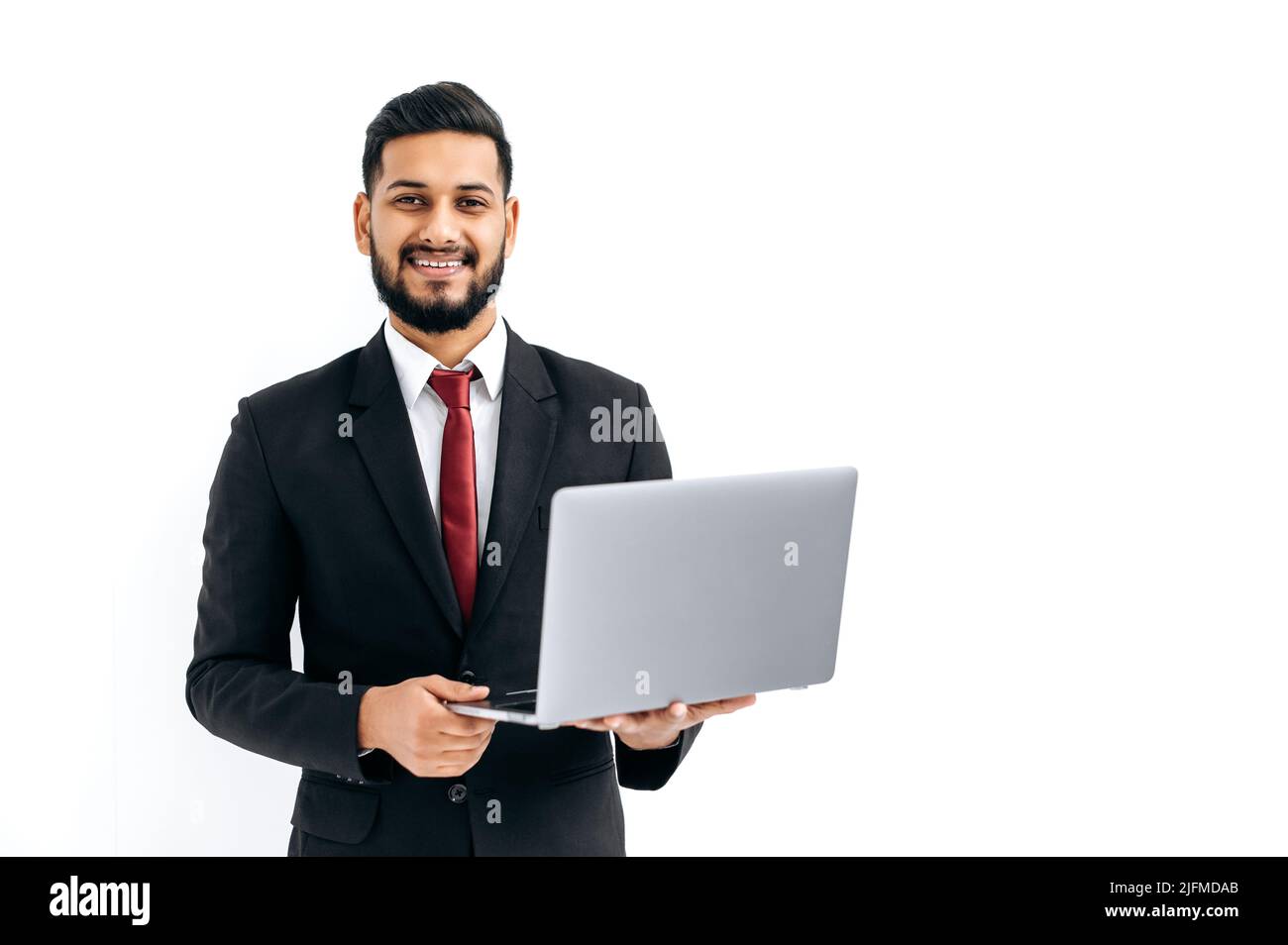 Erfolgreicher, gutaussehender indischer oder arabischer Mann im Business-Anzug, männlicher Unternehmer, der einen offenen Laptop in den Händen hält, auf die Kamera schaut, auf isolierten weißen Hintergrund steht und freundlich lächelt. Kopierbereich Stockfoto