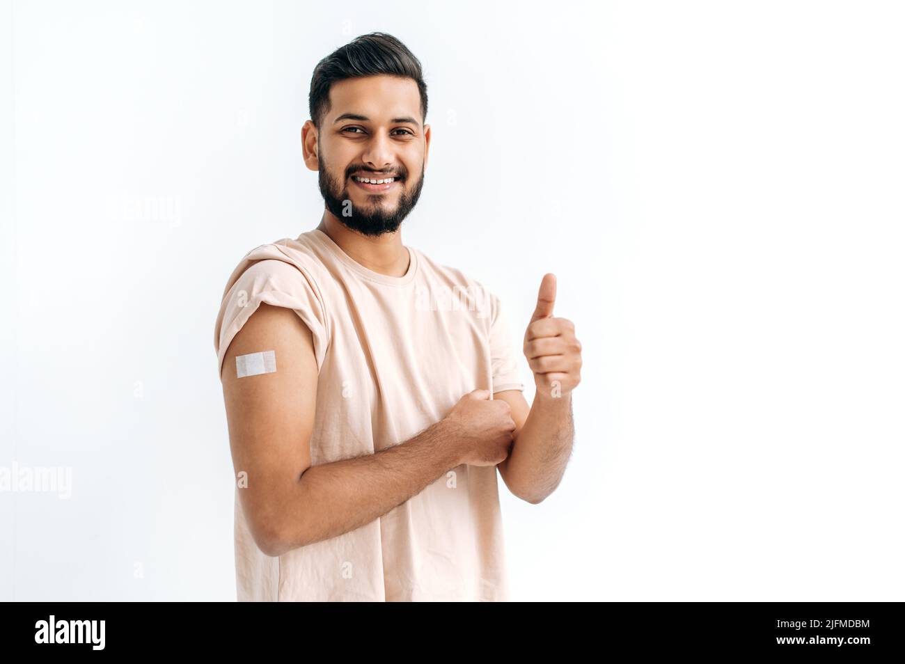 Impfungs- und Präventionskonzept. Positiver inder oder araber, der nach der Impfung Verbandsputz am Arm zeigt, Impfungen gegen Viren, auf isoliertem weißen Hintergrund steht, lächelt Stockfoto