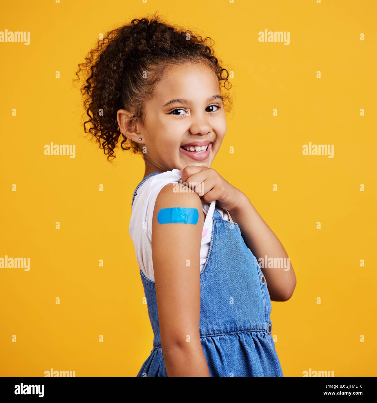 Studioportrait gemischtes Rennmädchen mit einem Gips auf ihrem Arm isoliert vor einem gelben Hintergrund. Niedliches hispanisch Kind, das ihren Ärmel hochhebt, um zu zeigen Stockfoto