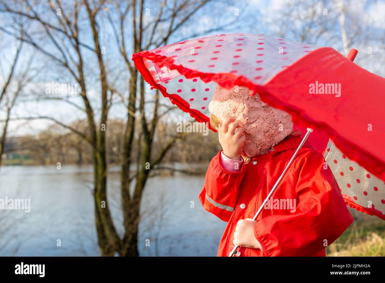 Kind spielt nach dem Regen mit Regenschirm in roten Gummistiefeln und Regenmantel. Stockfoto