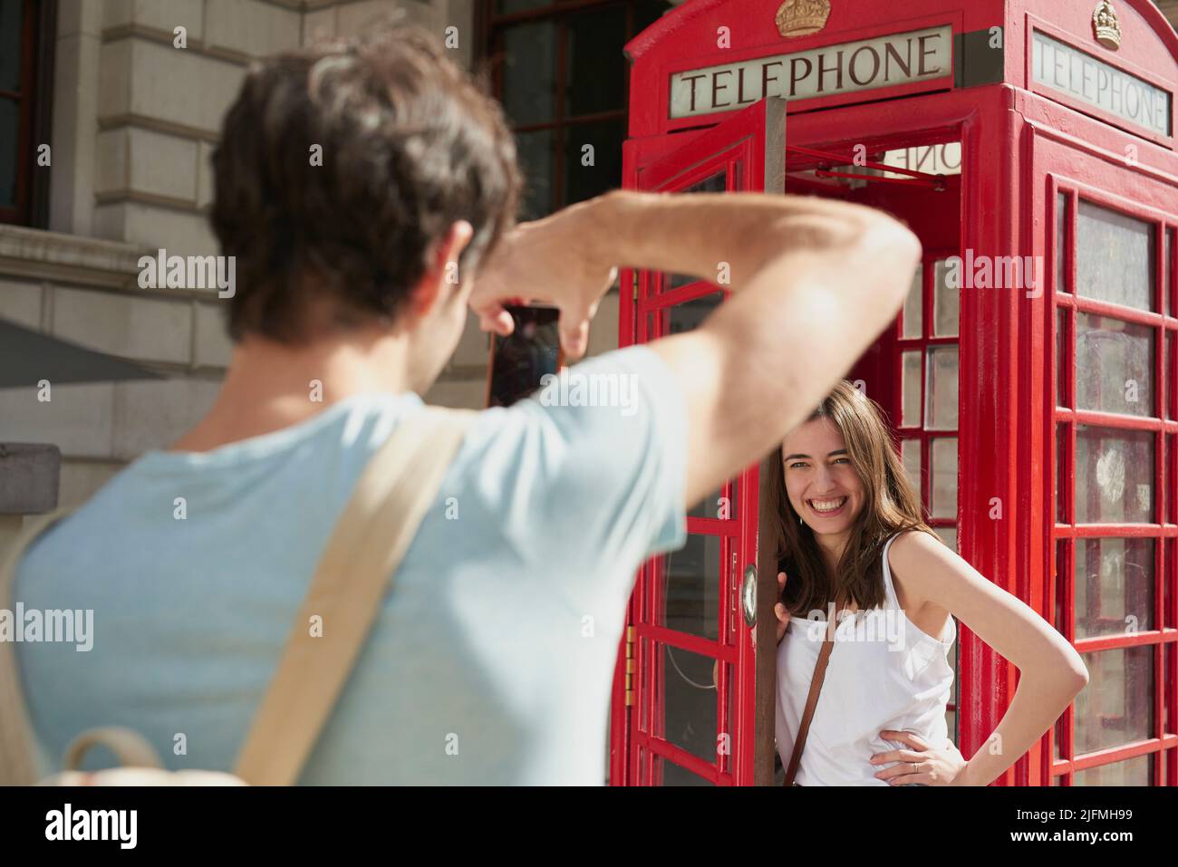 Du bist offiziell in London, wenn du eines davon siehst. Aufnahme eines jungen Mannes, der während der Aufnahme Fotos von seiner Freundin mit dem Smartphone in einer Telefonzelle machte Stockfoto