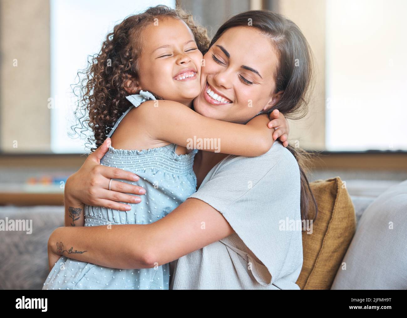 Liebevolle Mutter und Tochter umarmen sich gegenseitig, während sie zu Hause auf der Couch sitzen. Liebevolle Eltern und Kinder teilen zärtliche Momente Stockfoto