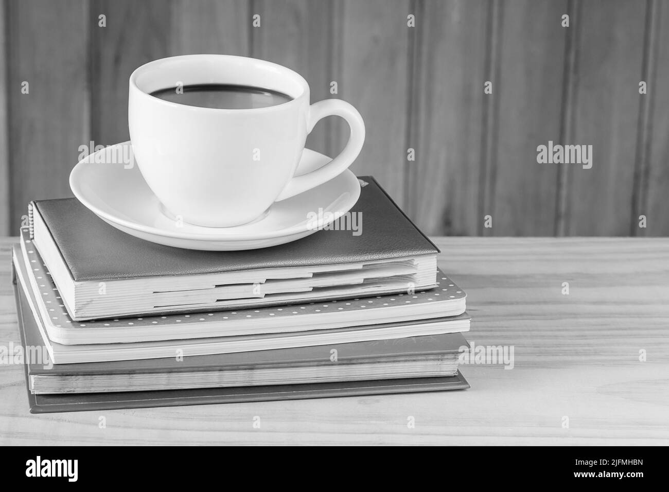 Tasse Kaffee und Notizbuch auf Holztisch Hintergrund.Schwarz-Weiß-Ton Stockfoto
