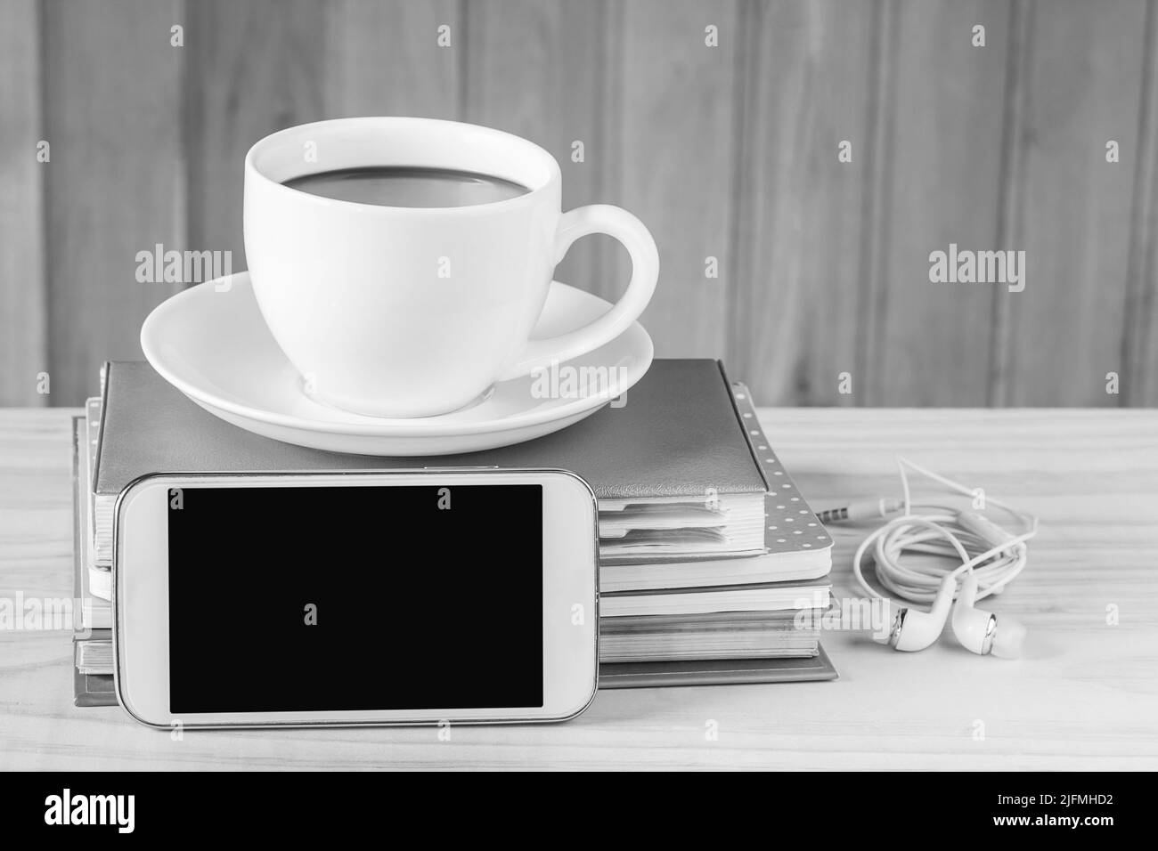 Smartphone und Kaffee mit Notizbuch auf Holztischhintergrund.Schwarz-Weiß-Ton Stockfoto