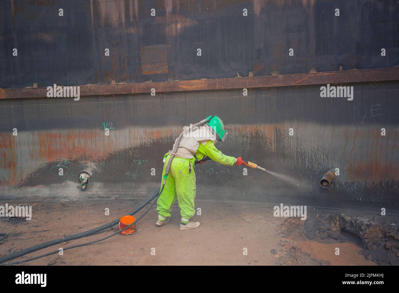 Weibliche Arbeiter Oberfläche Korrosionsplatte Vorbereitung durch Sandstrahlen des Tanks Innenöl Stockfoto