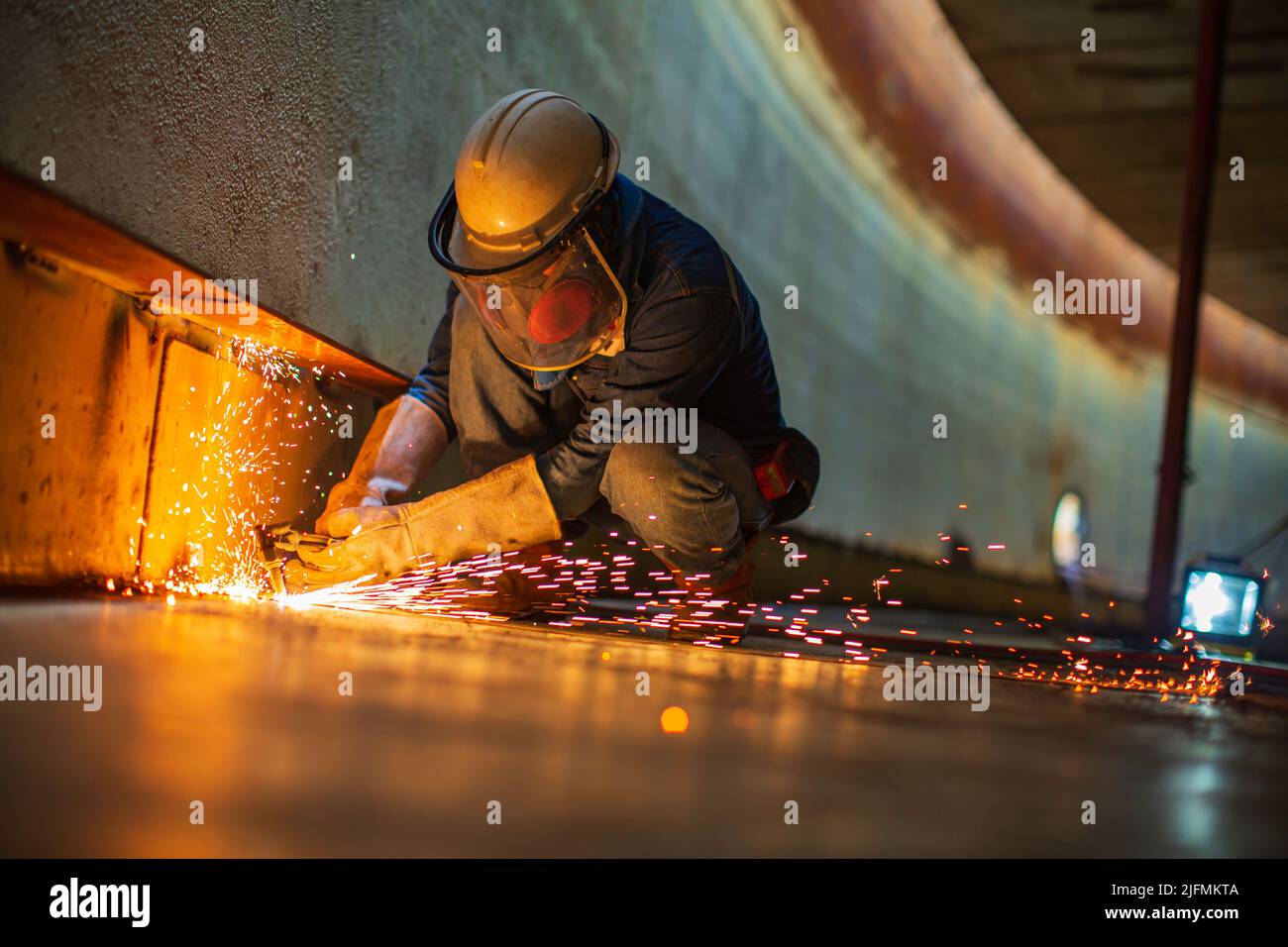 Metallspender des männlichen Arbeiters auf der Stahlplatte des Behälterbodens mit Blitzlicht in Nahaufnahme Schutzhandschuhe und Maske auf engem Raum tragen Stockfoto