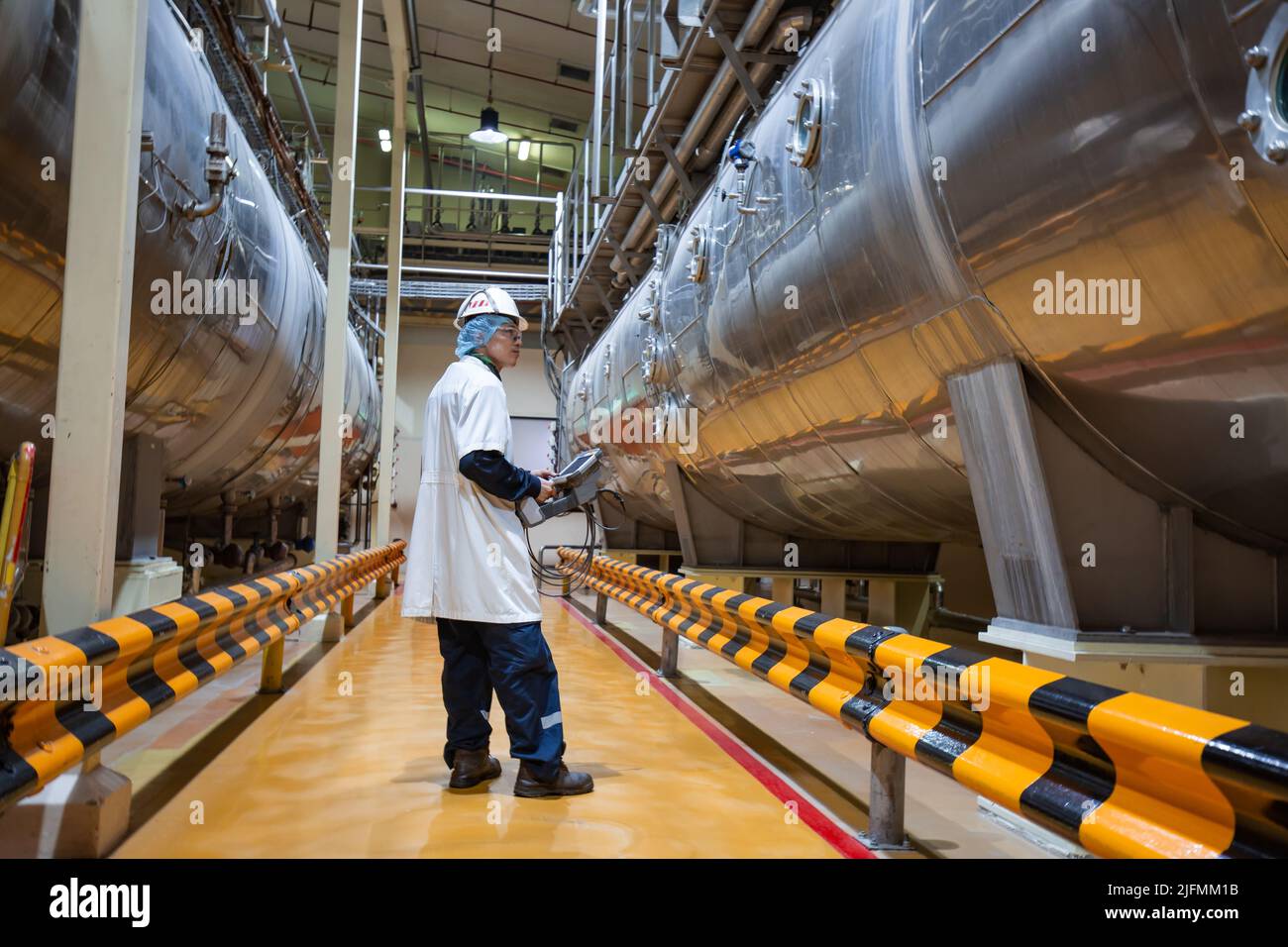 Männlicher Arbeitsinspektionsprozess Milchpulverkeller in der Fabrik mit horizontalen Edelstahltanks Stockfoto