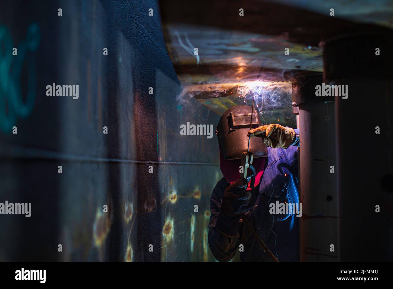 Schweißen männliche Arbeiter Metallbogen ist Teil der Maschinentank Düse Rohrleitung Bau Erdöl und Gas Lagertank in engen Räumen. Stockfoto