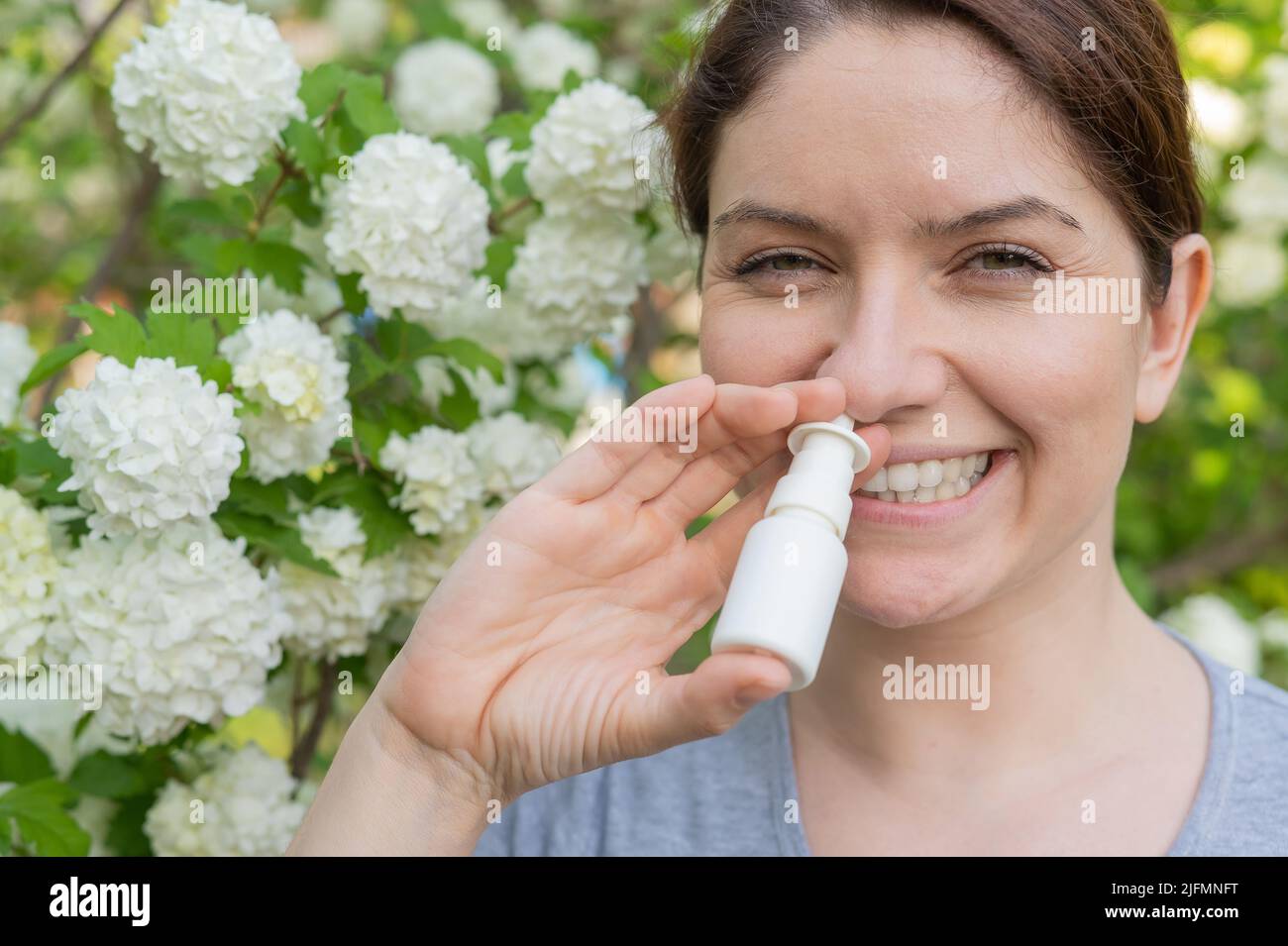 Kaukasische Frau verwendet ein Nasenspray, während sie im Park spazieren geht. Stockfoto