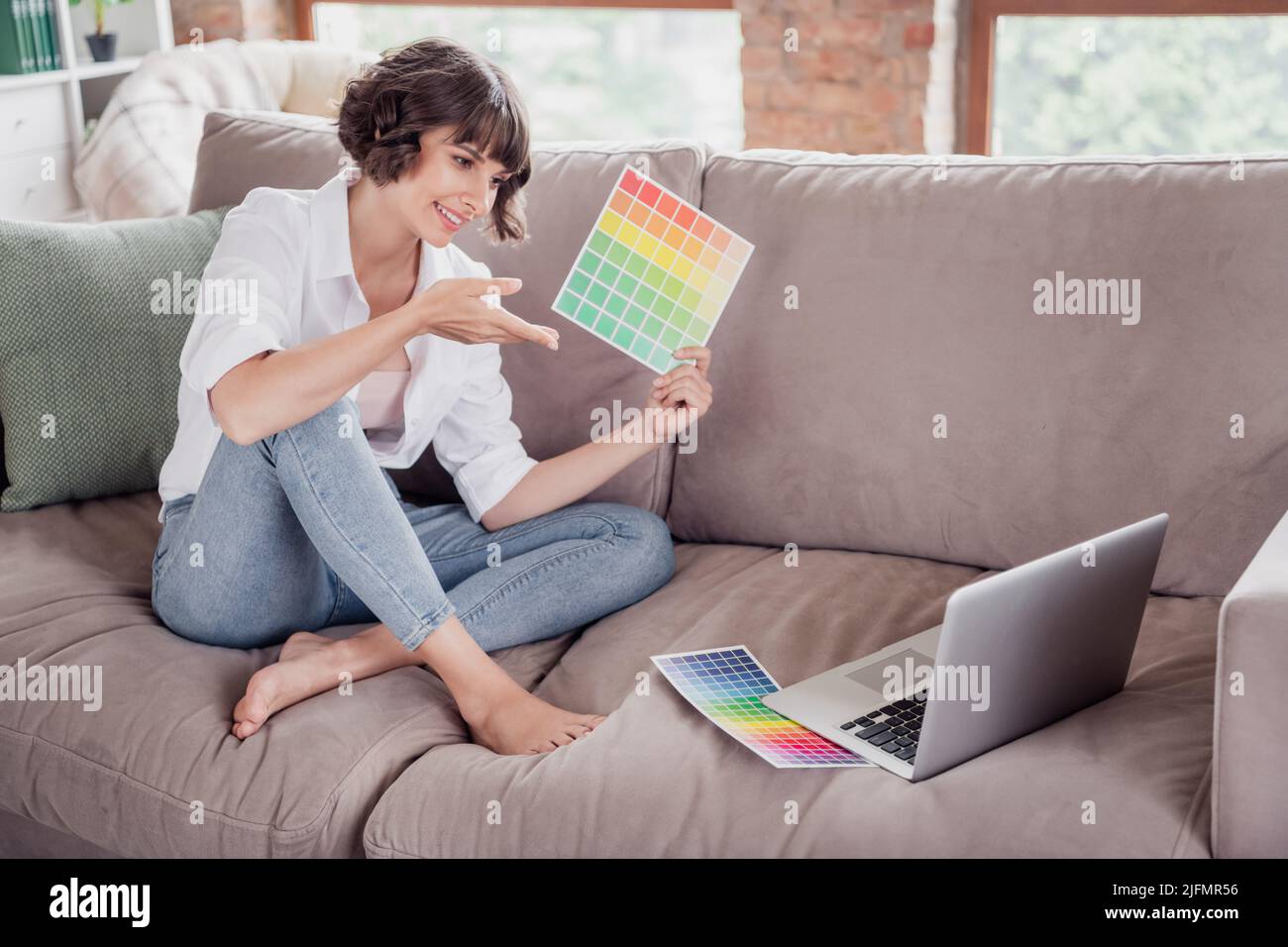 Foto in voller Länge in Körpergröße, weibliche Grafikdesignerin, die einen Laptop verwendet und Farbpaletten auf dem Videoanschluss zeigt Stockfoto