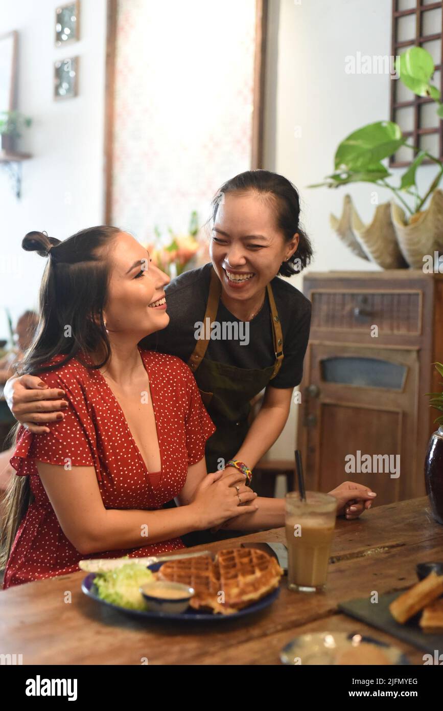 Junge vietnamesische Kellnerin lächelt und umarmt einen befreundeten Kunden Stockfoto